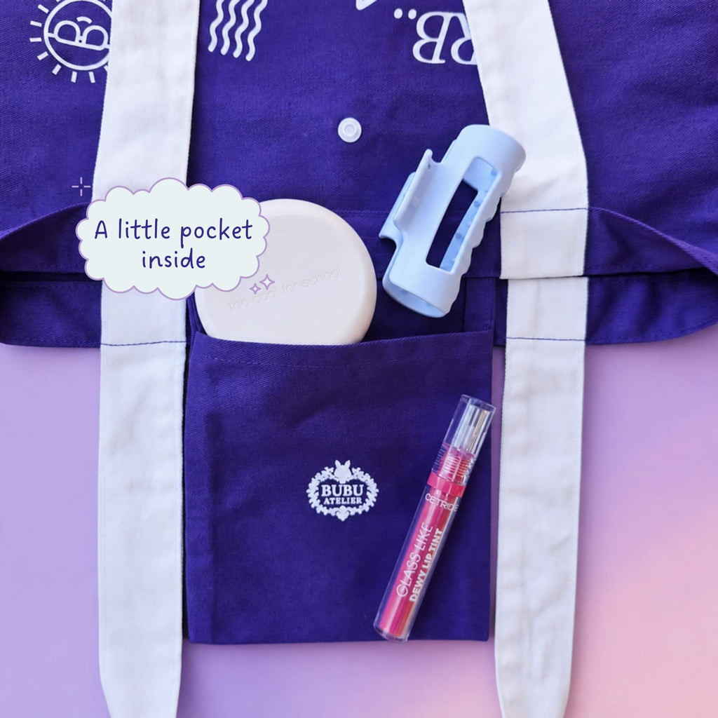A purple fabric pouch or pocket organizer with white straps, shown on a pink background. The pouch has a white embroidered logo reading 'BUBU STUDIO' and includes a text bubble that says 'A little pocket inside.